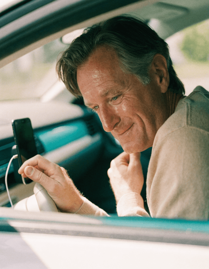A dad in the driver's seat, soft smile and wet eyes, hearing a song from a phone on the dashboard.