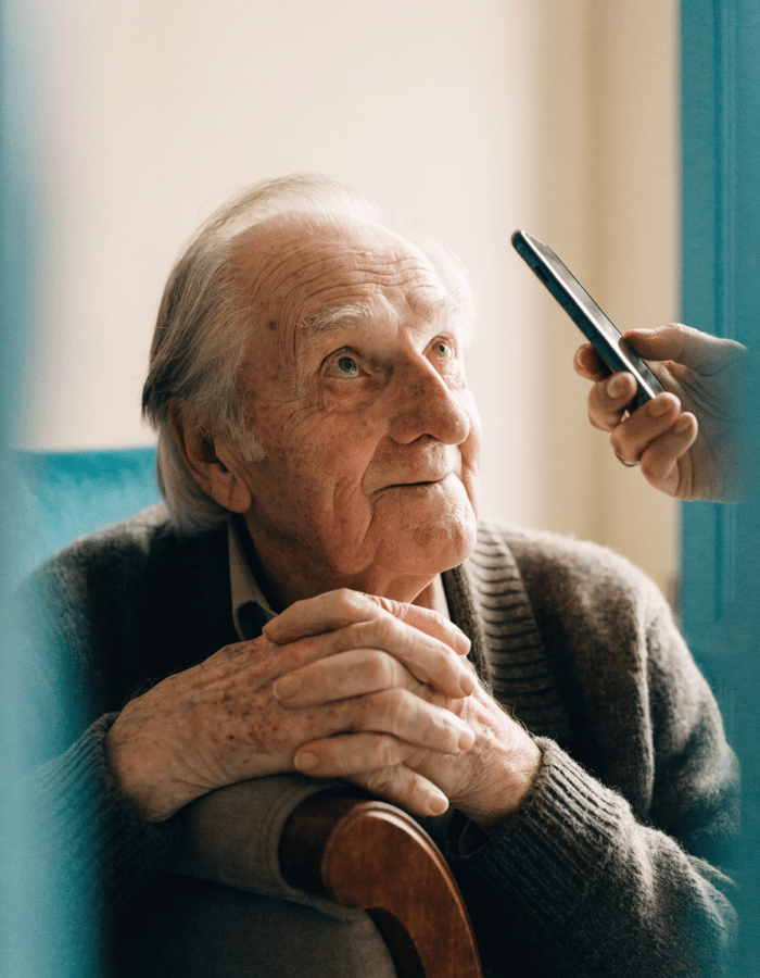 A grandad in an armchair, surprised gentle smile, hearing a song from a phone nearby.