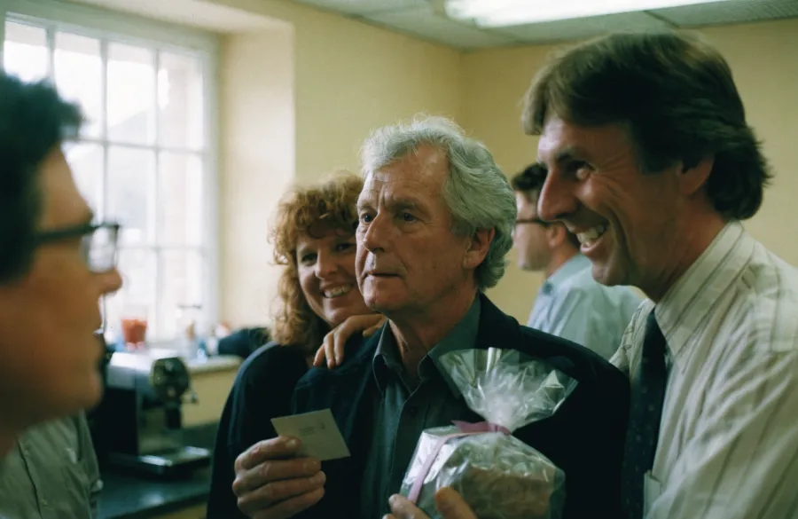 A man on his last day at work holding a card and a gift, surrounded by smiling colleagues.